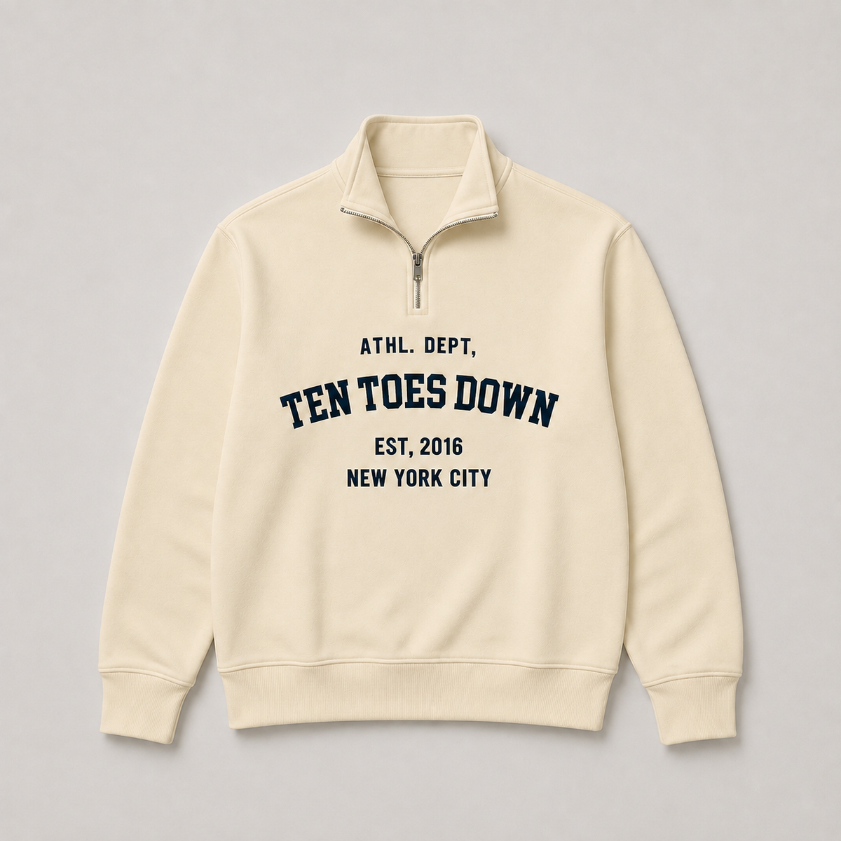 A cream-colored quarter-zip sweatshirt with oversized navy blue text reading " TEN TOES DOWN"
