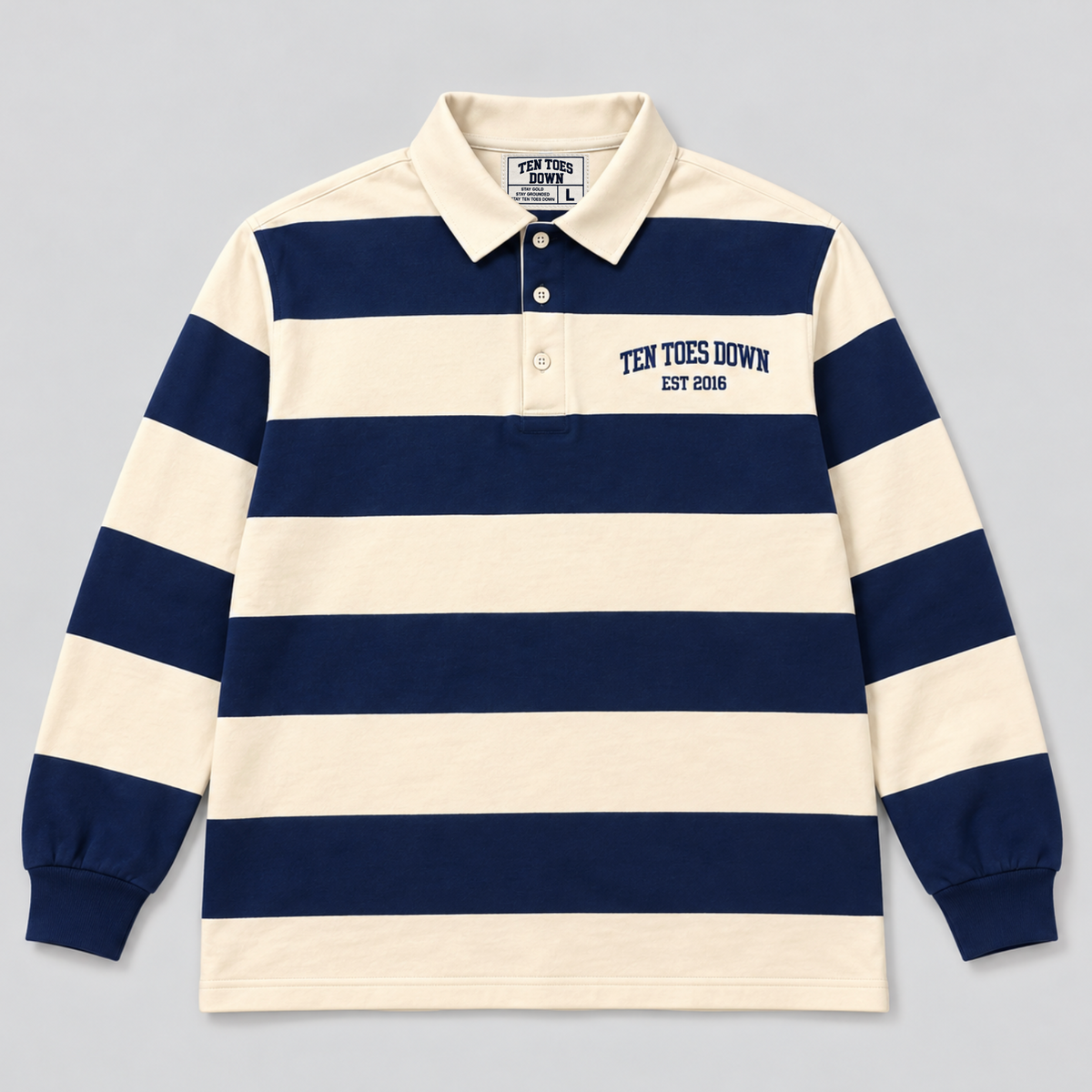 A long-sleeve polo shirt with horizontal navy blue and cream stripes, featuring 'TEN TOES DOWN EST 2016' printed on the left chest. The shirt is laid flat against a neutral gray background.